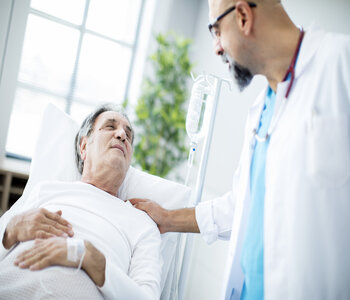 Male Physician is smiling at an elderly male patient that is lying down in a patient bed.
